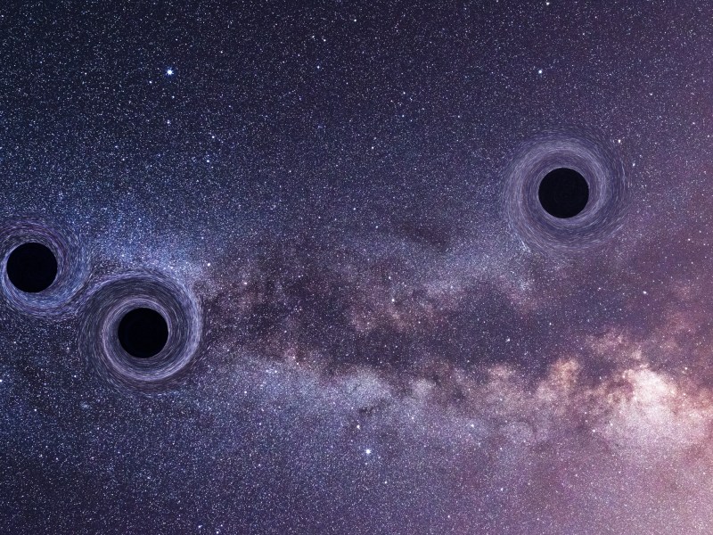 A photo illustration of three black holes on a starry sky background.